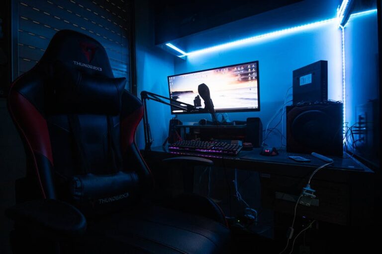 A sleek gaming desk with a monitor, gaming chair, and LED lights creating an immersive environment.