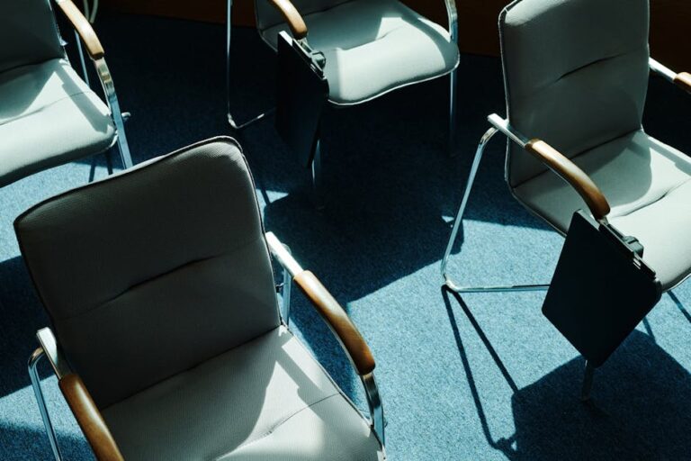 A view from above of empty chairs casting shadows in a sunlit office meeting room.