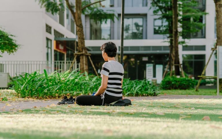 A woman meditating in a city park, surrounded by greenery on a sunny day.
