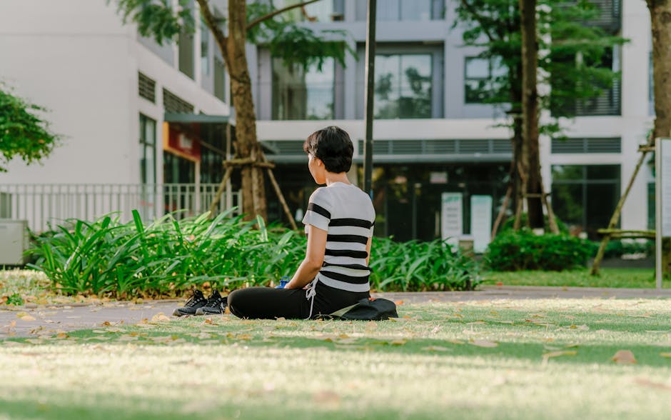 A woman meditating in a city park, surrounded by greenery on a sunny day.