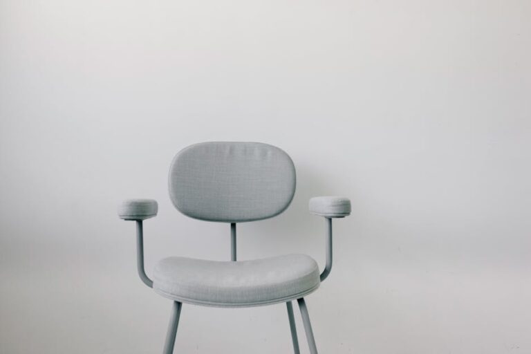 Elegant grey armchair with armrests placed in front of a sleek white wall, ideal for modern interiors.