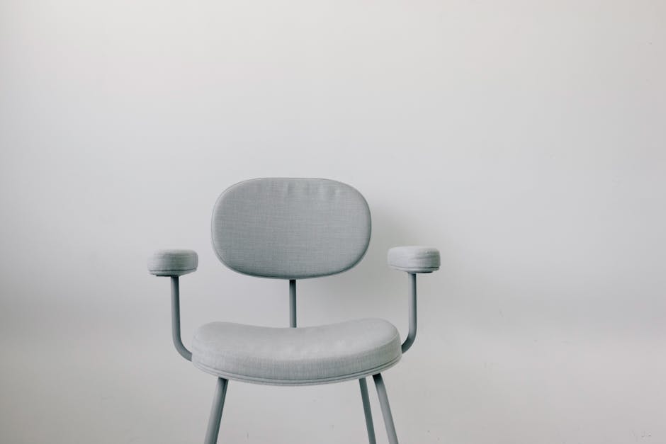 Elegant grey armchair with armrests placed in front of a sleek white wall, ideal for modern interiors.