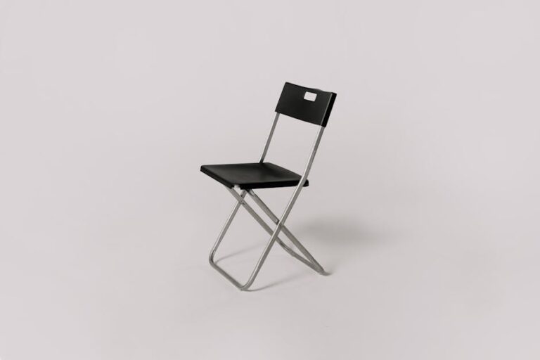 Minimalistic photo of a black folding chair against a plain gray background, ideal for studio shoot representation.