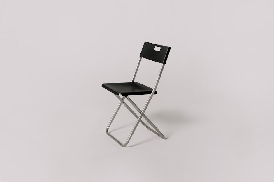 Minimalistic photo of a black folding chair against a plain gray background, ideal for studio shoot representation.