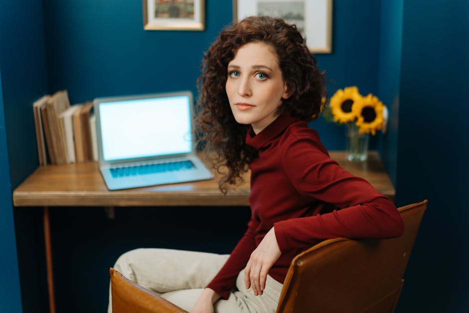 Woman with curly hair sitting at desk with laptop and sunflowers in cozy home office.