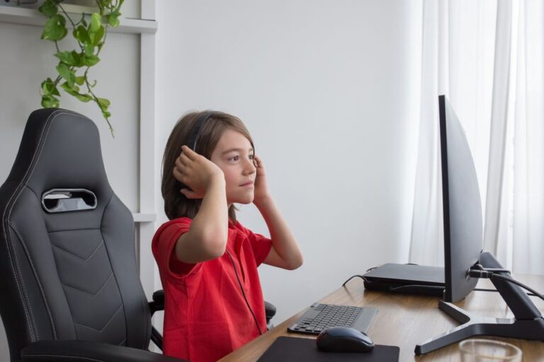 a young boy in a red shirt sits at a computer desk wearing h